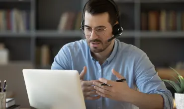 Icono de hombre con audífonos y micrófonos sosteniendo una video llamada en notebook
